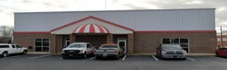 Brick building with red and white awning with four vechiles park out front of the building.